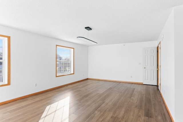 unfurnished room featuring a textured ceiling, baseboards, and wood finished floors