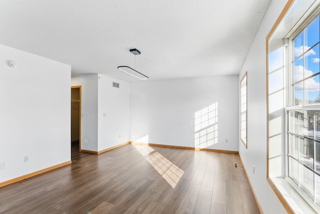 spare room with a textured ceiling, wood finished floors, visible vents, and baseboards