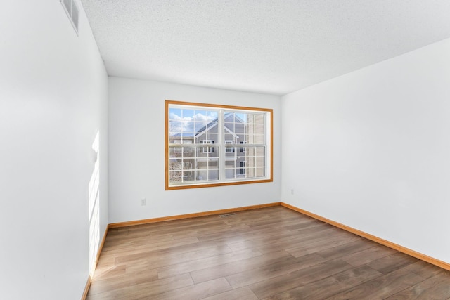 spare room with baseboards, a textured ceiling, visible vents, and wood finished floors