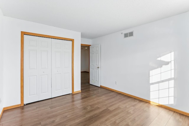 unfurnished bedroom with a closet, visible vents, baseboards, and wood finished floors