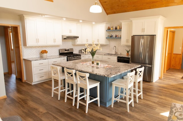 kitchen featuring stainless steel appliances, under cabinet range hood, a sink, vaulted ceiling, and a kitchen bar