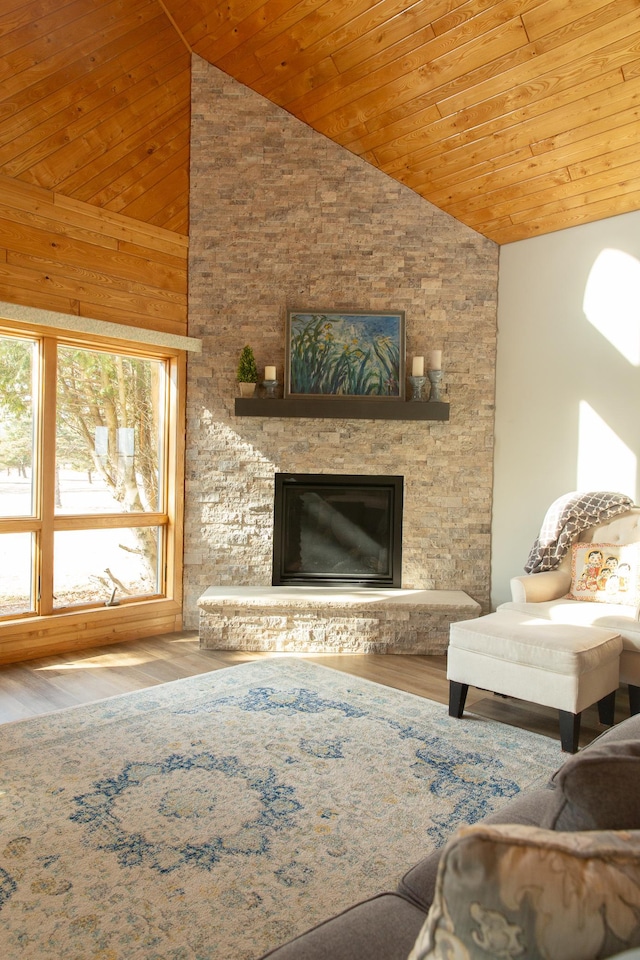 living room featuring vaulted ceiling, wooden ceiling, wood finished floors, and a stone fireplace