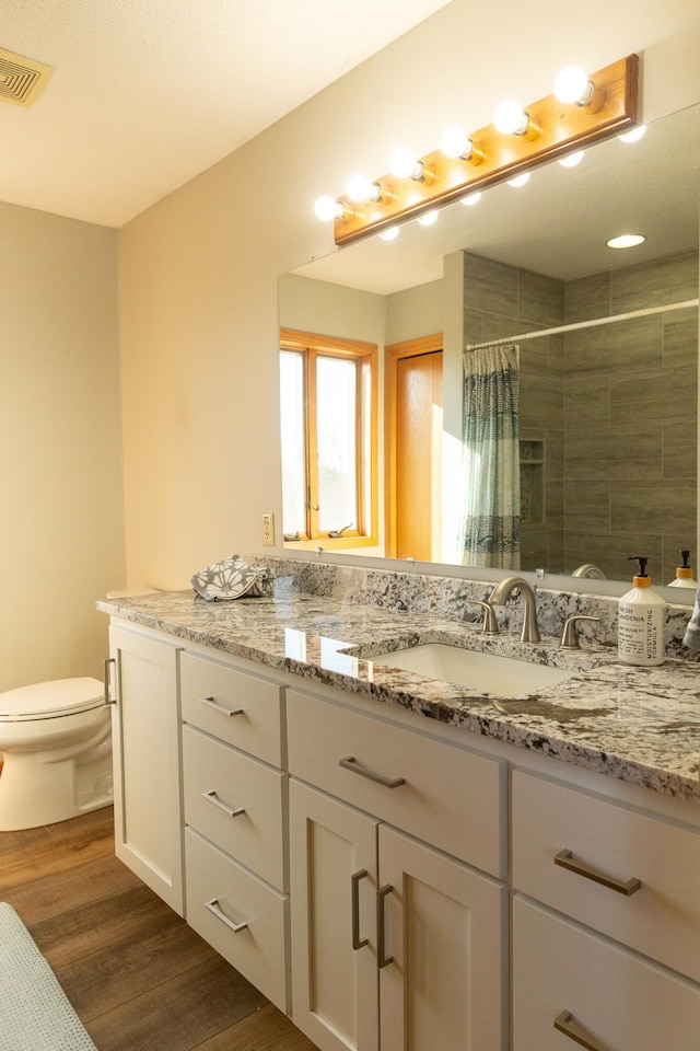 bathroom featuring wood finished floors, toilet, tiled shower, and vanity