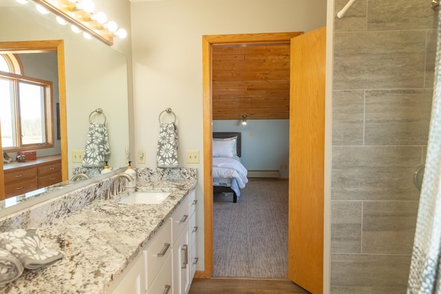 ensuite bathroom featuring vanity, baseboards, a baseboard heating unit, and tiled shower