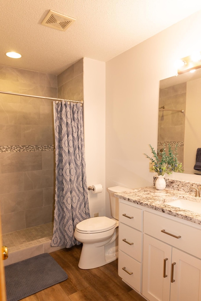 bathroom featuring wood finished floors, tiled shower, toilet, vanity, and a textured ceiling