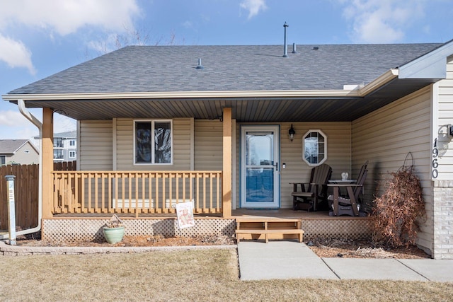 view of exterior entry featuring covered porch, roof with shingles, and fence