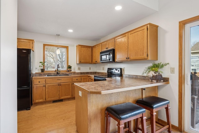 kitchen with a breakfast bar, recessed lighting, a peninsula, black appliances, and a sink