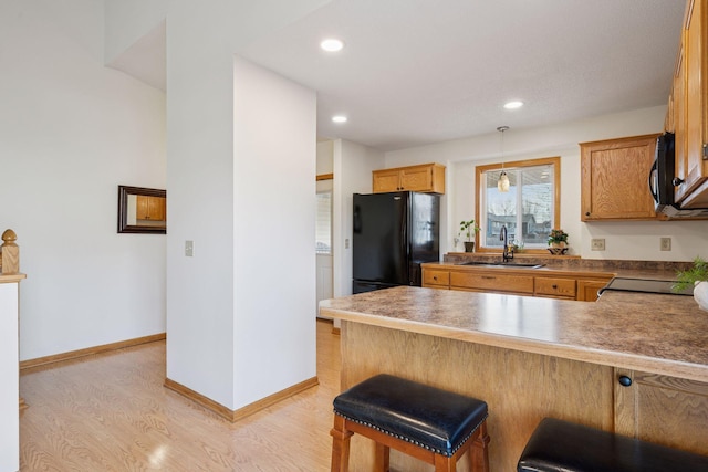 kitchen with baseboards, light wood-type flooring, a peninsula, black appliances, and a sink