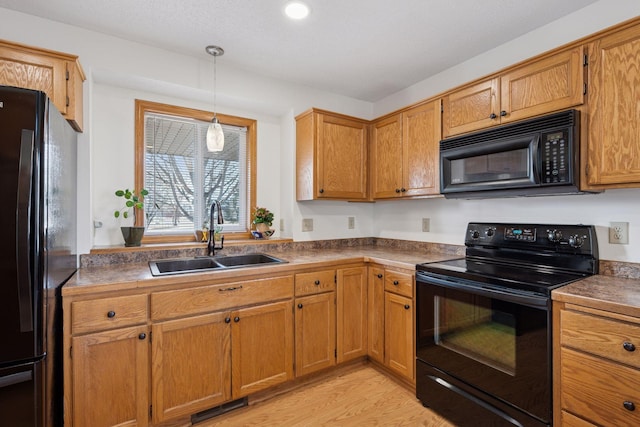 kitchen featuring light wood finished floors, visible vents, hanging light fixtures, black appliances, and a sink