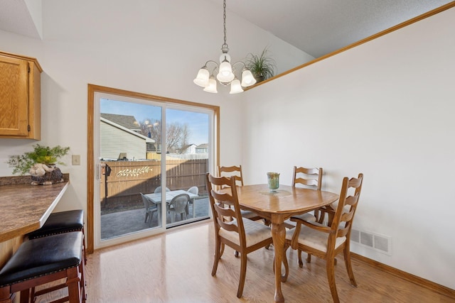 dining area featuring a chandelier, visible vents, light wood-style flooring, and lofted ceiling