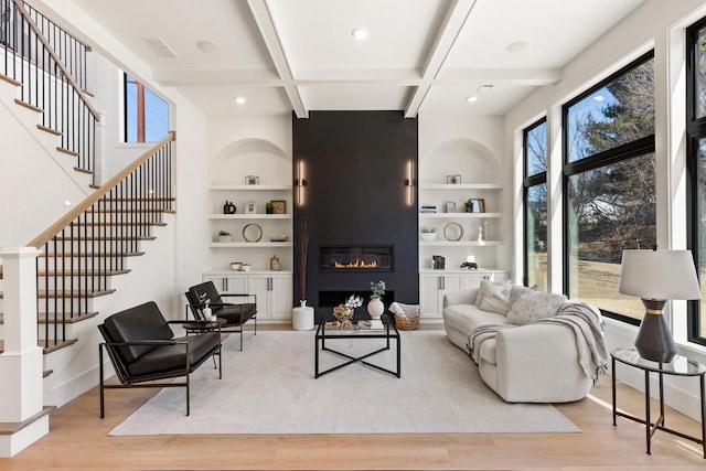 living room featuring built in shelves, coffered ceiling, a fireplace, light wood-style floors, and beamed ceiling