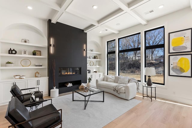 living area featuring built in shelves, a fireplace, coffered ceiling, visible vents, and light wood-type flooring