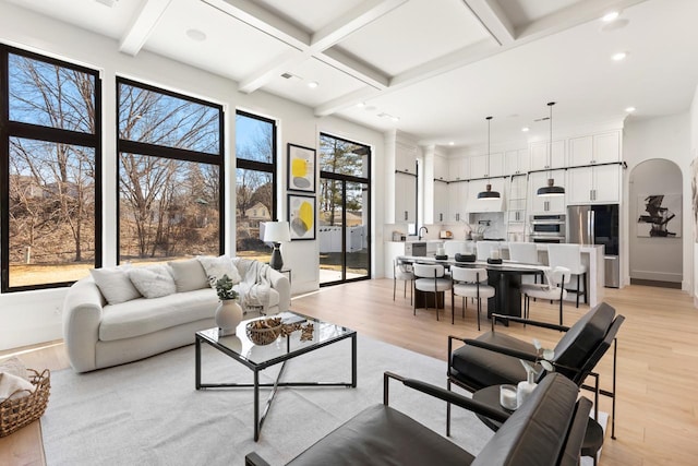 living room featuring arched walkways, coffered ceiling, beamed ceiling, light wood-type flooring, and recessed lighting