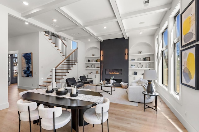 dining space with coffered ceiling, stairway, light wood-type flooring, a fireplace, and beam ceiling