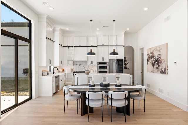 dining area featuring light wood-style floors, arched walkways, and visible vents