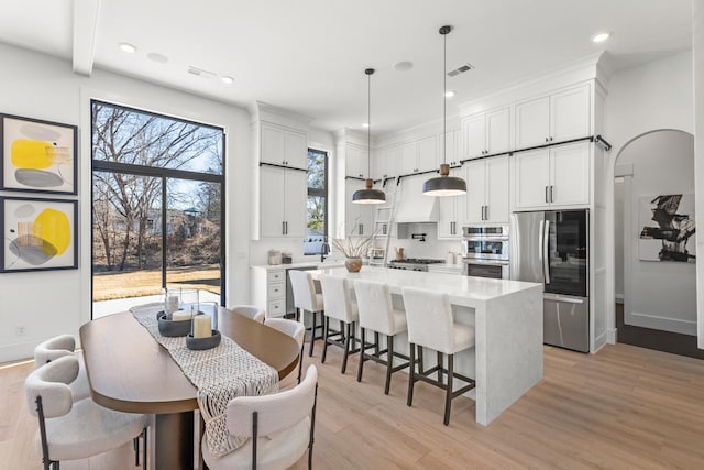 kitchen featuring arched walkways, stainless steel appliances, white cabinetry, a center island, and light wood finished floors