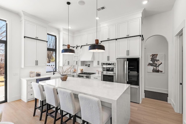 kitchen with arched walkways, custom exhaust hood, visible vents, appliances with stainless steel finishes, and white cabinets