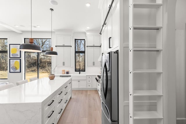 kitchen featuring freestanding refrigerator, white cabinetry, a sink, and light wood-style flooring