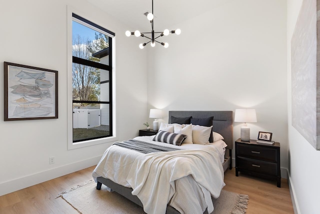 bedroom with baseboards, light wood-type flooring, and an inviting chandelier