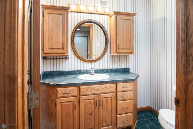 half bathroom featuring vanity, toilet, baseboards, and visible vents