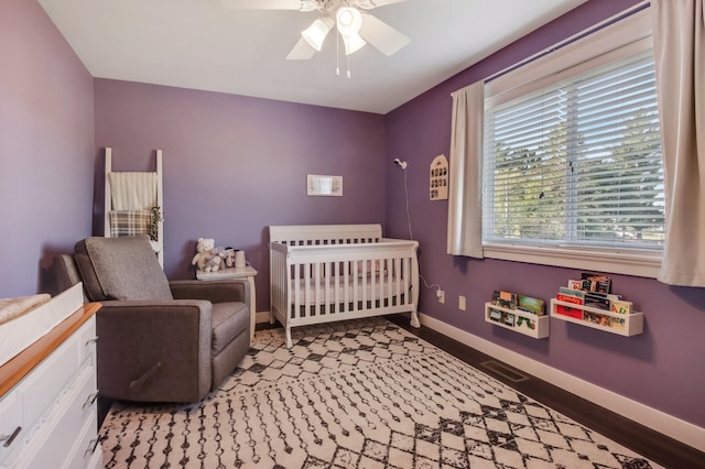 bedroom featuring a nursery area, baseboards, and a ceiling fan