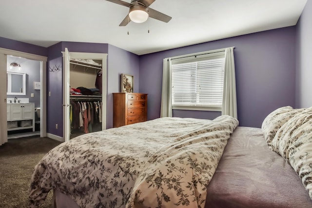 bedroom featuring a walk in closet, dark colored carpet, a closet, a sink, and baseboards