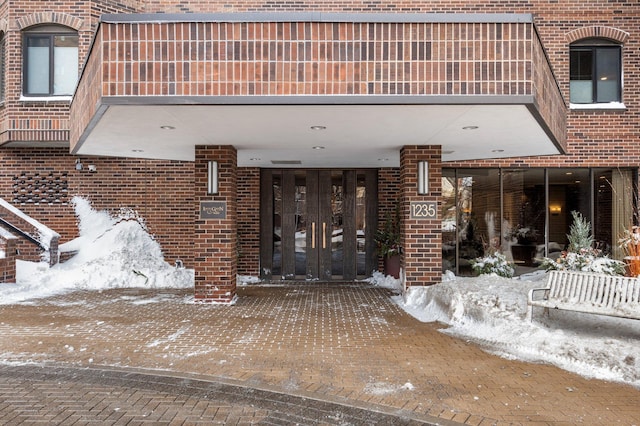 snow covered property entrance with brick siding and french doors