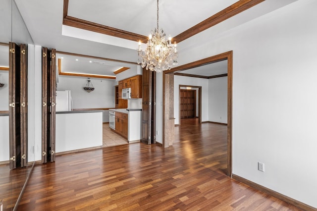 unfurnished dining area featuring baseboards, a raised ceiling, wood finished floors, and crown molding