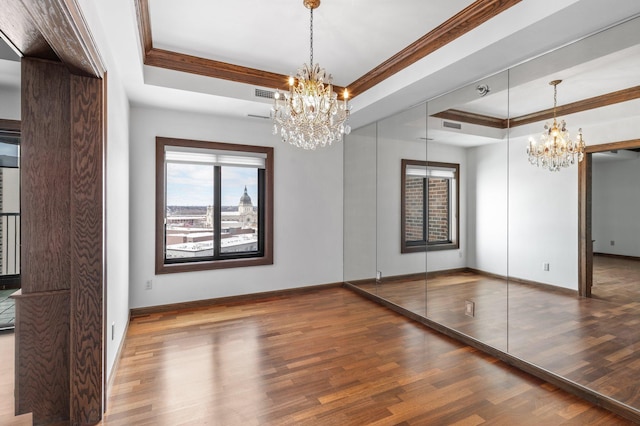 unfurnished dining area featuring visible vents, a raised ceiling, a notable chandelier, and wood finished floors