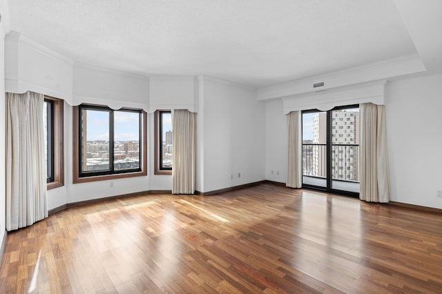 spare room with baseboards, a textured ceiling, wood finished floors, and crown molding