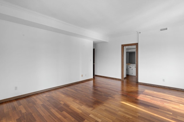 empty room with crown molding, wood finished floors, visible vents, and baseboards