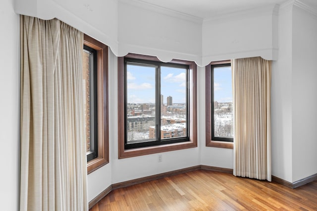 empty room featuring light wood-type flooring, baseboards, a view of city, and crown molding