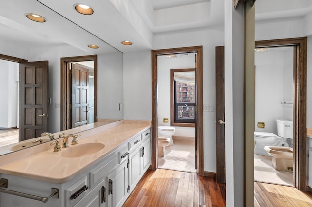 bathroom with vanity, wood finished floors, toilet, and a bidet