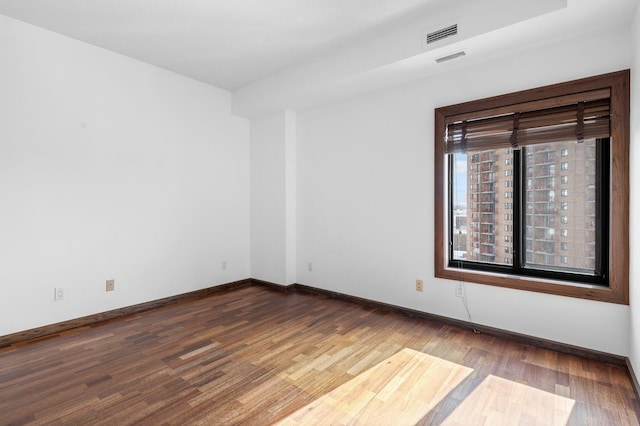 unfurnished room with visible vents, wood finished floors, and baseboards