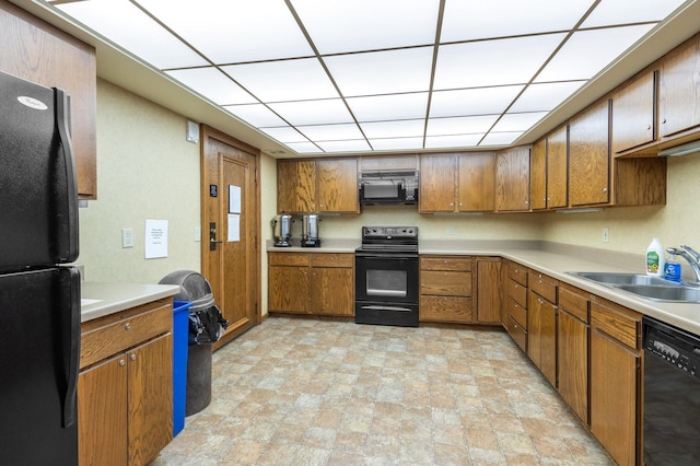 kitchen featuring brown cabinets, black appliances, a sink, a drop ceiling, and light countertops