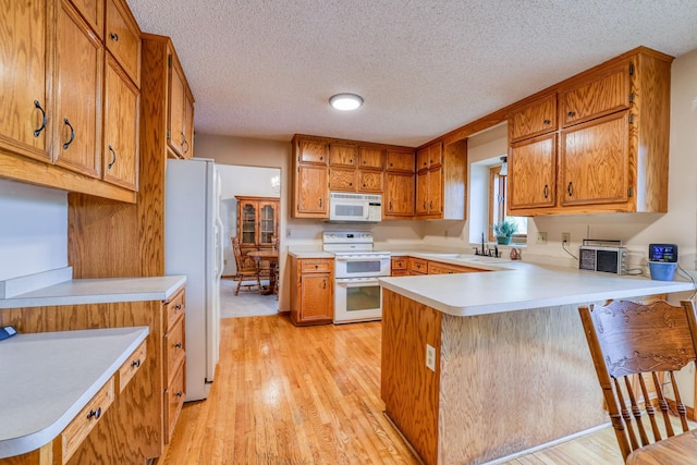 kitchen with white appliances, brown cabinets, a peninsula, light countertops, and a sink
