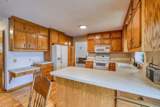 kitchen featuring white appliances, light countertops, a sink, and a peninsula