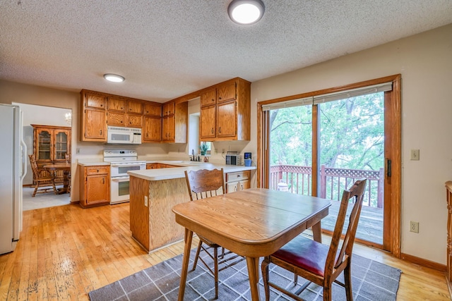 kitchen with white appliances, light wood finished floors, brown cabinetry, a peninsula, and light countertops
