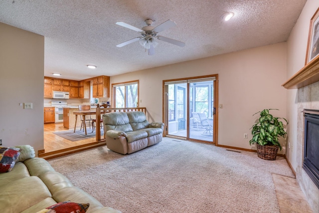 living room featuring light colored carpet, ceiling fan, a textured ceiling, a tile fireplace, and baseboards
