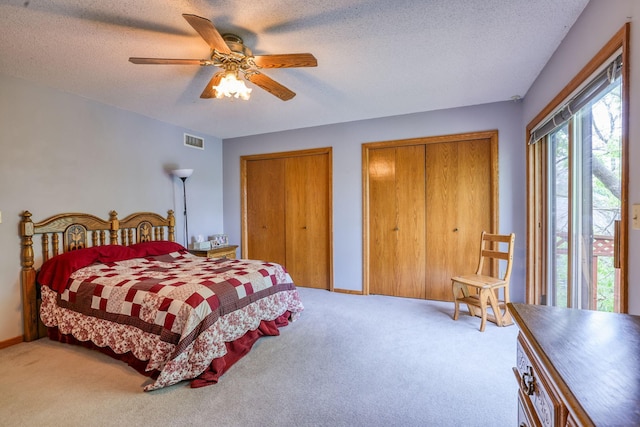 carpeted bedroom with a textured ceiling, a ceiling fan, baseboards, visible vents, and multiple closets