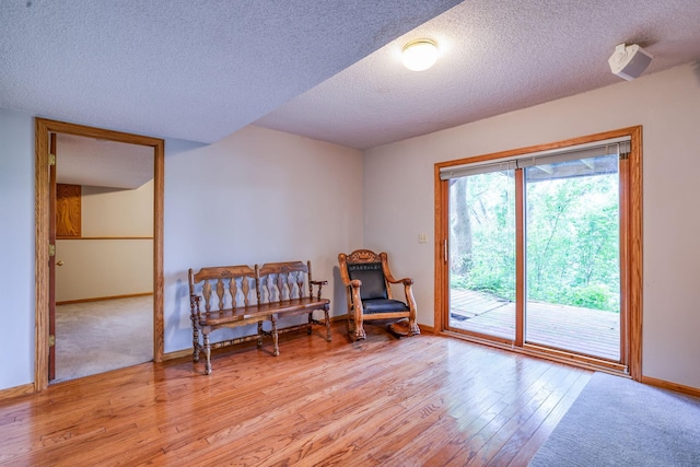 living area featuring a textured ceiling, light wood-type flooring, and baseboards