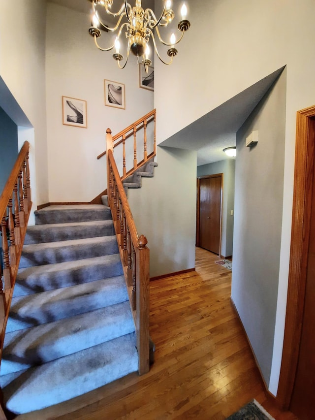 staircase featuring a chandelier, a high ceiling, wood finished floors, and baseboards