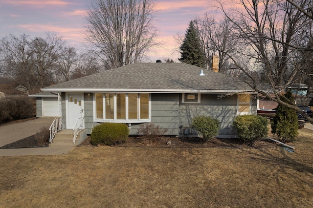 single story home featuring a garage, roof with shingles, a chimney, and a yard