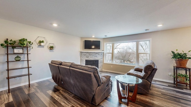 living area featuring dark wood-style floors, a stone fireplace, and baseboards