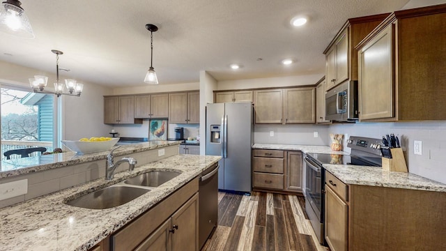 kitchen featuring light stone counters, dark wood-style flooring, a sink, stainless steel appliances, and decorative light fixtures