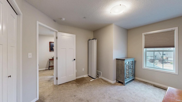 unfurnished bedroom with baseboards, light carpet, a textured ceiling, and visible vents