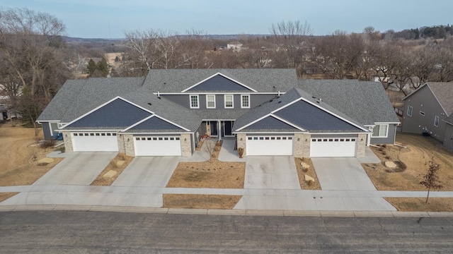 view of front of house with concrete driveway, stone siding, a garage, and roof with shingles