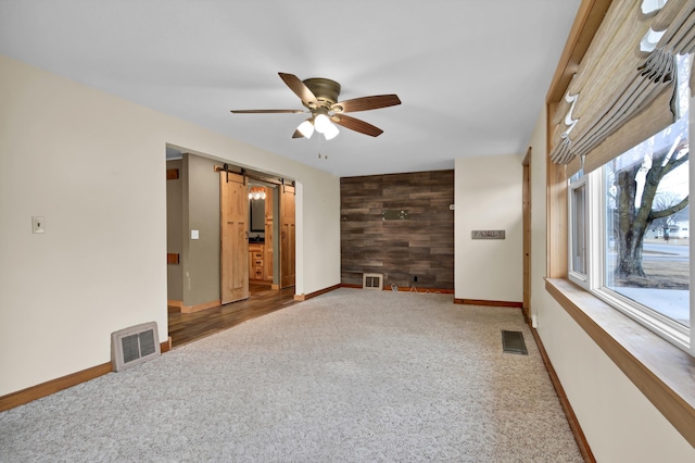 empty room with a barn door, carpet floors, an accent wall, wood walls, and visible vents