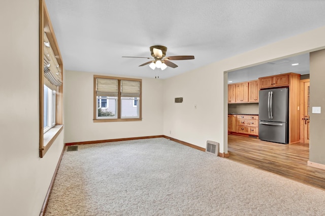 unfurnished living room featuring visible vents, a ceiling fan, light colored carpet, and baseboards