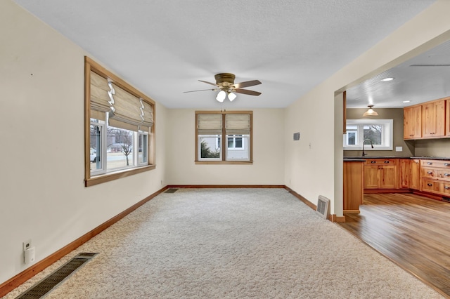 unfurnished living room with a ceiling fan, visible vents, and baseboards